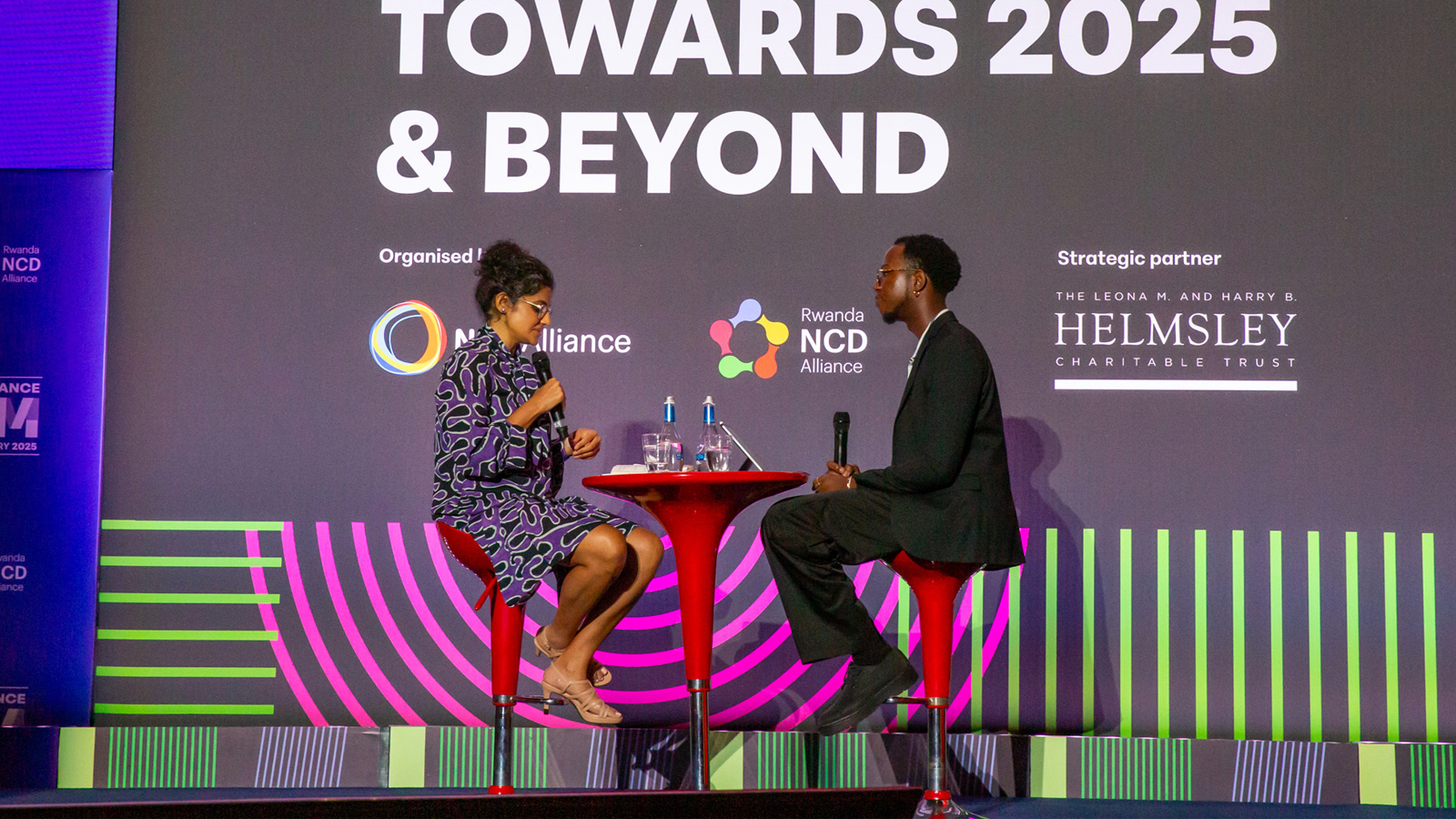 Two people on stage with a microphone talking ncd financing at the ncd alliance forum in kigali 2025