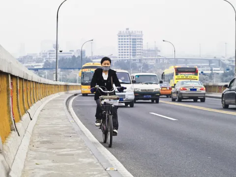 woman rides a bicycle on a road full of cars and pollution in China