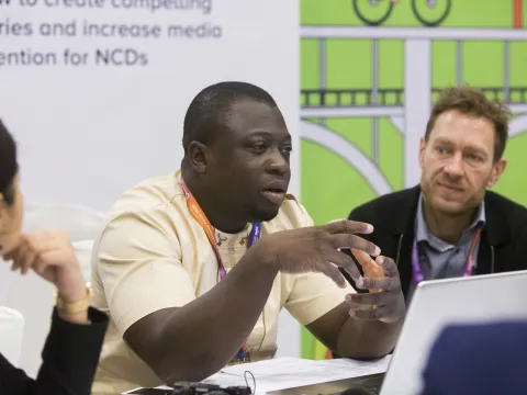 NCD Advocate Christ Agbega speaking into a microphone at an event 
