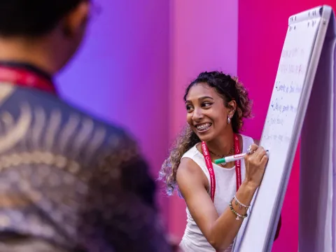 Young woman at Global NCD Alliance Forum 2025 smiling and writing on whiteboard