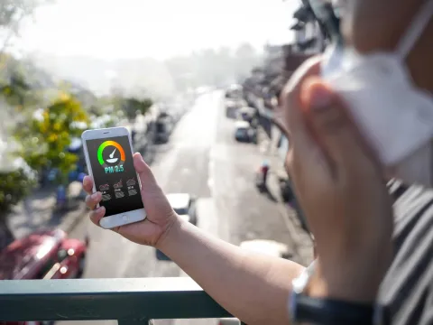 A person checks real-time air pollution levels on their smartphone while wearing a protective mask outdoors
