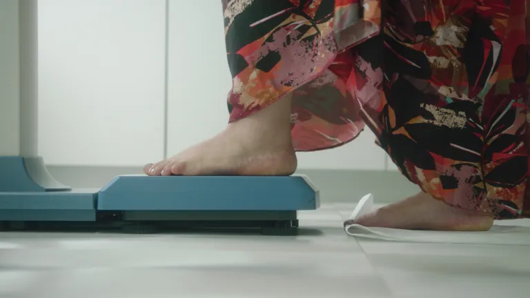 Close up of person stepping on a scale. Still from 'From small steps to systemic shifts' from the Turning the Tide series