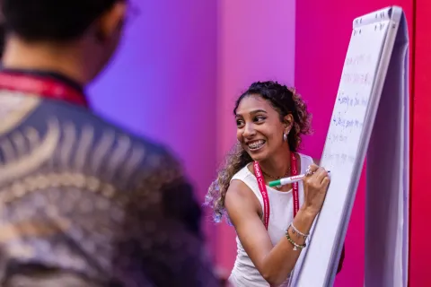 Young woman at Global NCD Alliance Forum 2025 smiling and writing on whiteboard